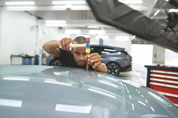 Ein Mitarbeiter der BMW Werkstatt beim Smart Repair der Motorhaube.