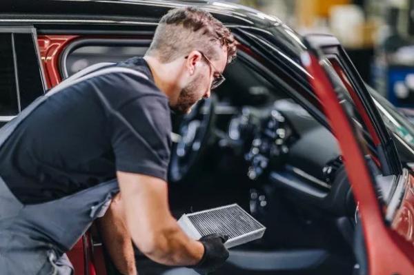 Ein Servicemitarbeiter einer MINI Werkstatt tauscht den Luftpartikelfilter einer Belüftung eines orangenen MINI Coopers.