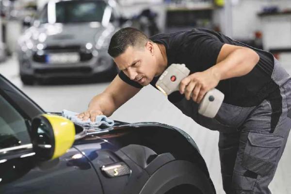 Ein Mitarbeiter eine MINI Servicewerkstatt prüft den Lack der Motorhaube eines schwarzen MINIs mit einer Lampe.